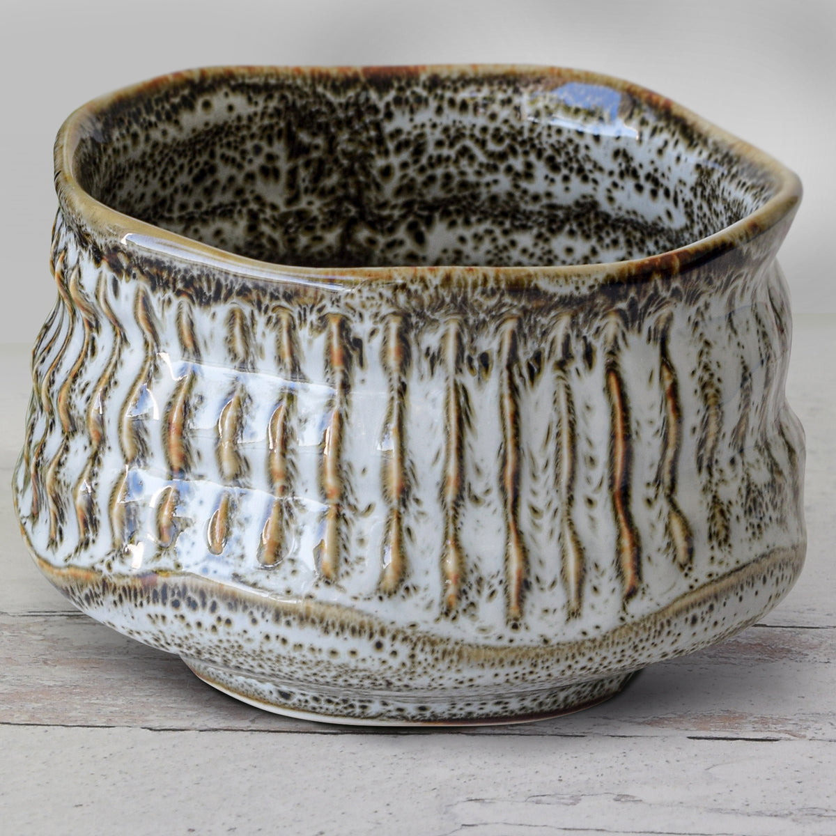 The White Ceramic Meisen Matcha Bowl, with a speckled glaze and irregular rim, elegantly pairs with a bamboo matcha whisk from the Organic Japanese Matcha Set, all resting on a light wooden surface.