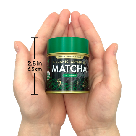 Hands holding a small tin of Organic Japanese Ceremonial Grade Matcha Green Tea Powder with a green lid, labeled "2.5 in, 6.5 cm.