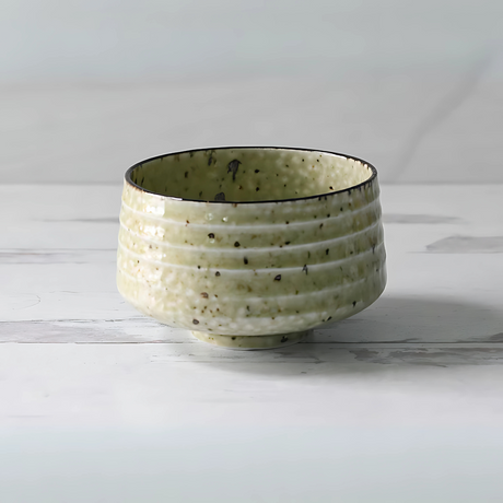 The Kaneni White Ceramic Matcha Bowl is a textured, green ceramic piece with a speckled pattern, reminiscent of traditional Japanese pottery. It perfectly complements any matcha accessory collection.