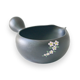 The Black Flowers Ceramic Matcha Bowl with Spout, adorned with floral designs on a black background and featuring a side handle, makes an ideal housewarming gift for admirers of the Japanese tea ceremony.
