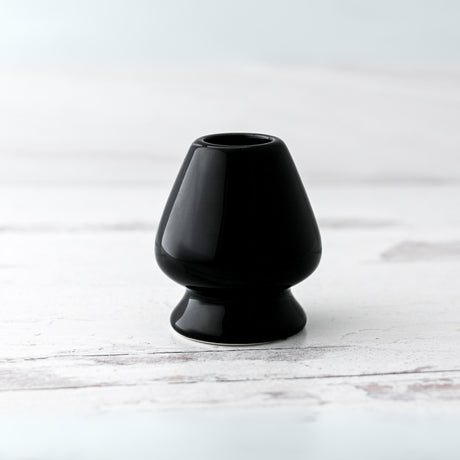 A Black Matcha Whisk Holder from the Bamboo Whisk Set, echoing a Japanese aesthetic, sits elegantly on a white wooden surface.