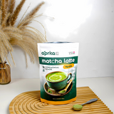 A bag of Ceremonial Grade Matcha Latte Powder Mix with Natural Vanilla Flavor sits on a wooden mat, accompanied by a matcha whisk and pampas grass in the background.