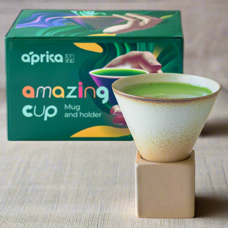 A green drink in a vintage-style brown coffee mug with a square base, featuring colorful packaging in the background.