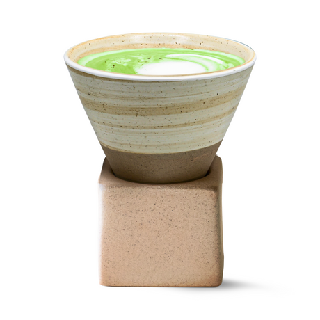 A Beige Coffee Mug with Base cradles a green and white matcha latte, elegantly resting on its square stone base.
