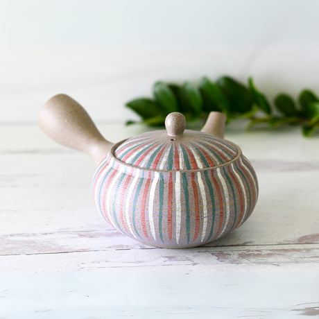 The Handcrafted Japanese Kyusu Teapot with Filters (310ml) rests on a light surface, with a green leaf in the background, illustrating the elegance of Japanese ceramics.