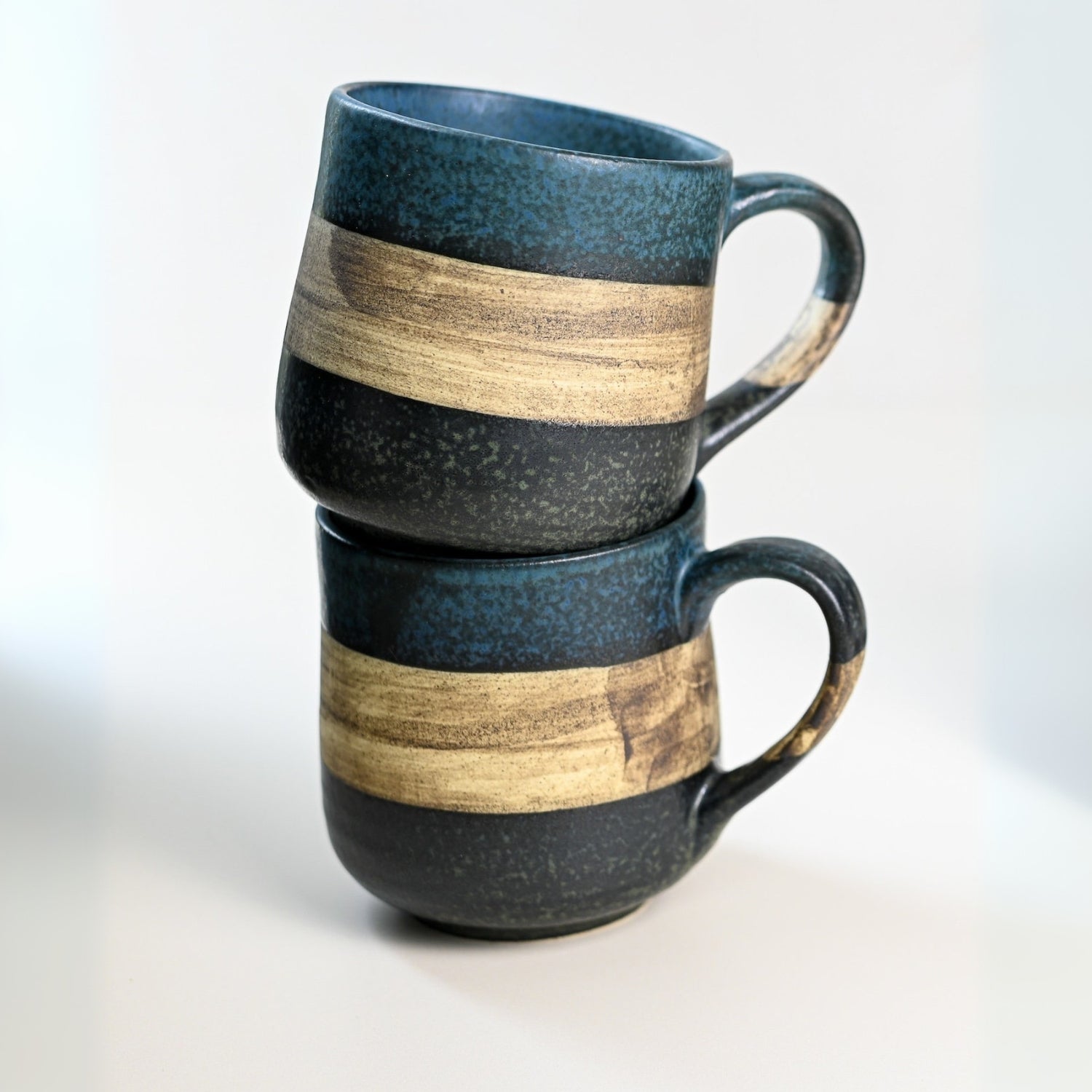 Two Handcrafted Mino Ware Ceramic Mugs from Japan, featuring wide beige bands and an 8 oz capacity, are artfully stacked on a white surface.