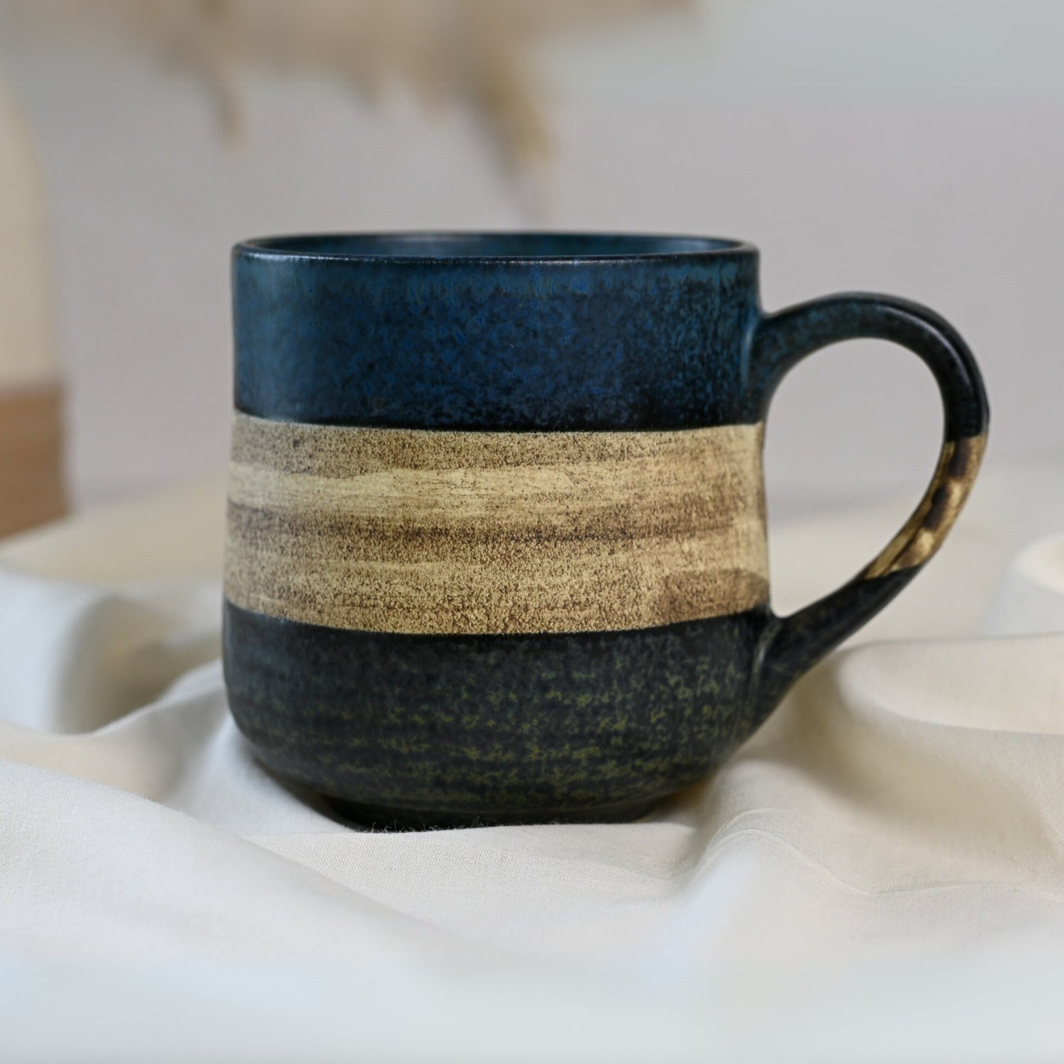 A Handcrafted Mino Ware Ceramic Mug from Japan, 8 oz (240 ml), in blue with a beige horizontal stripe, rests elegantly on a light cloth, showcasing traditional Japanese craftsmanship.