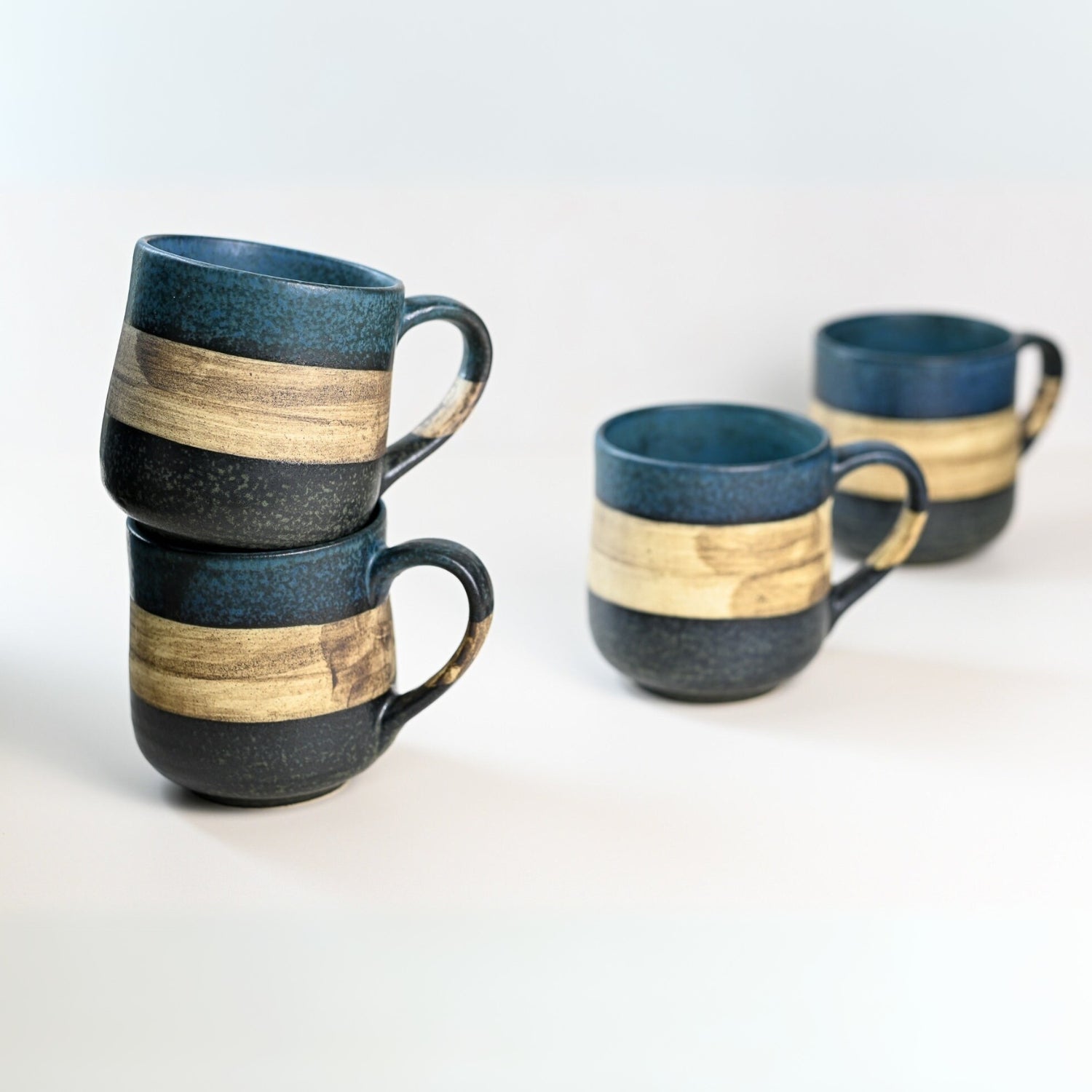 Two stacked and two single handcrafted Mino Ware ceramic mugs, each 8 oz, featuring blue and beige stripes, grace a white background, showcasing the elegance of Japanese craftsmanship.