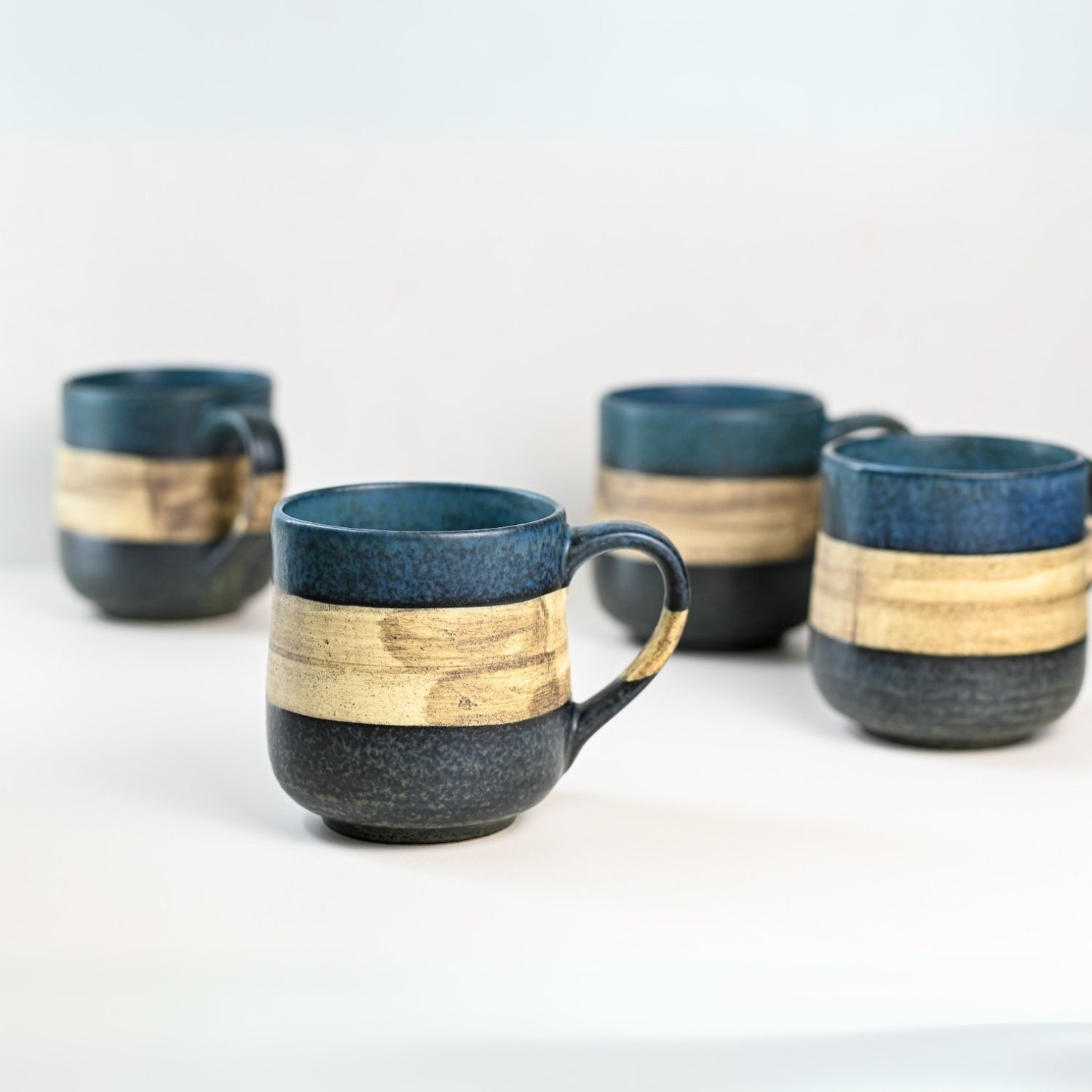Four Handcrafted Mino Ware Ceramic Mugs from Japan, each 8 oz (240 ml), featuring blue and beige bands, are displayed elegantly on a white surface, embodying the timeless artistry of Japanese pottery.
