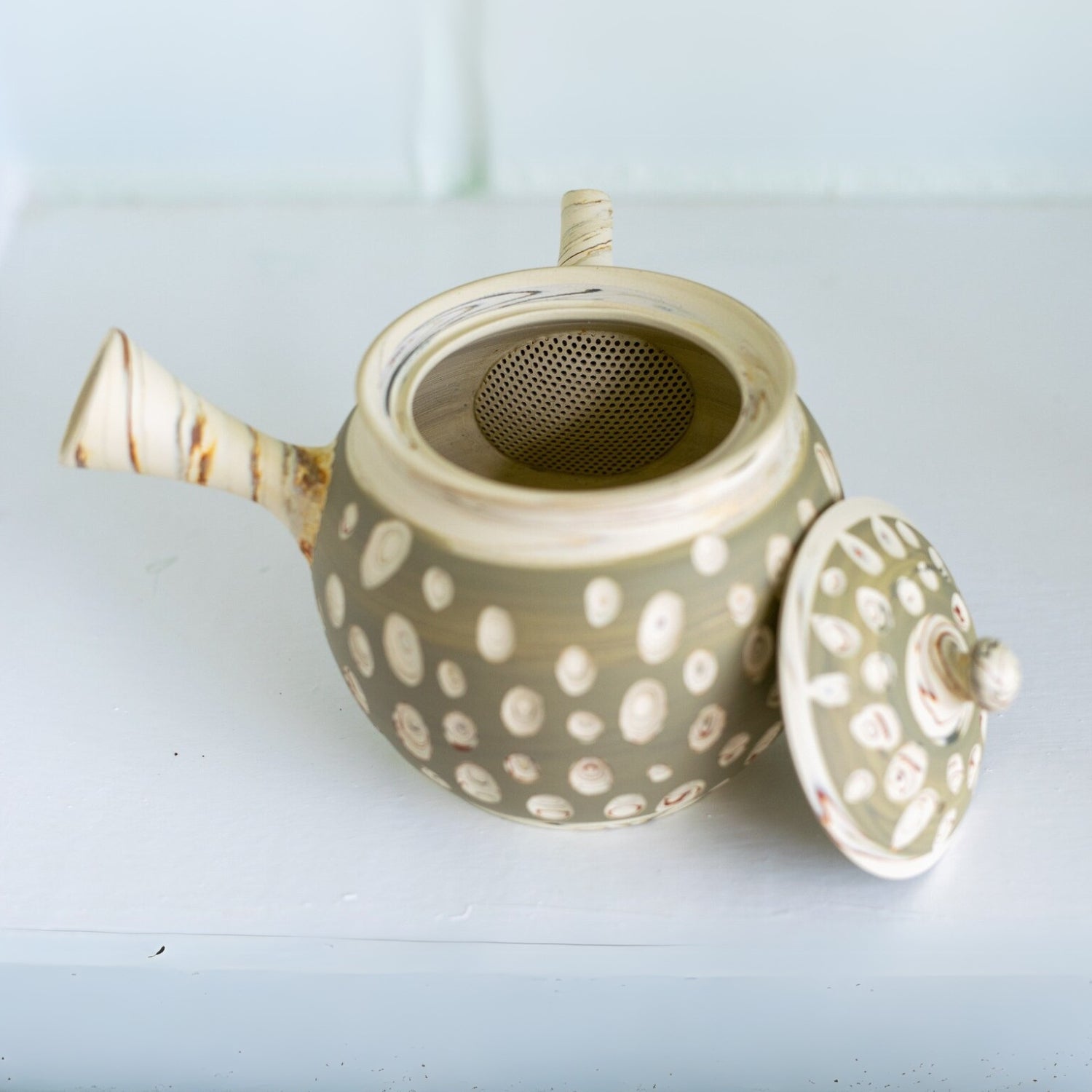 A beautiful Japanese Kyusu Set, featuring a ceramic teapot crafted from Tokoname clay with a dotted design, sits gracefully open on a white surface, ready to infuse delicate green tea flavors.