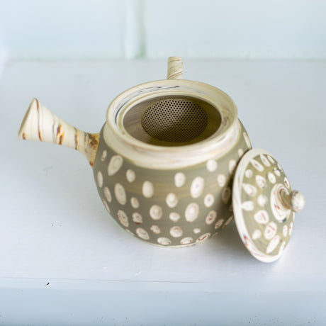 A beautiful Japanese Kyusu Set, featuring a ceramic teapot crafted from Tokoname clay with a dotted design, sits gracefully open on a white surface, ready to infuse delicate green tea flavors.