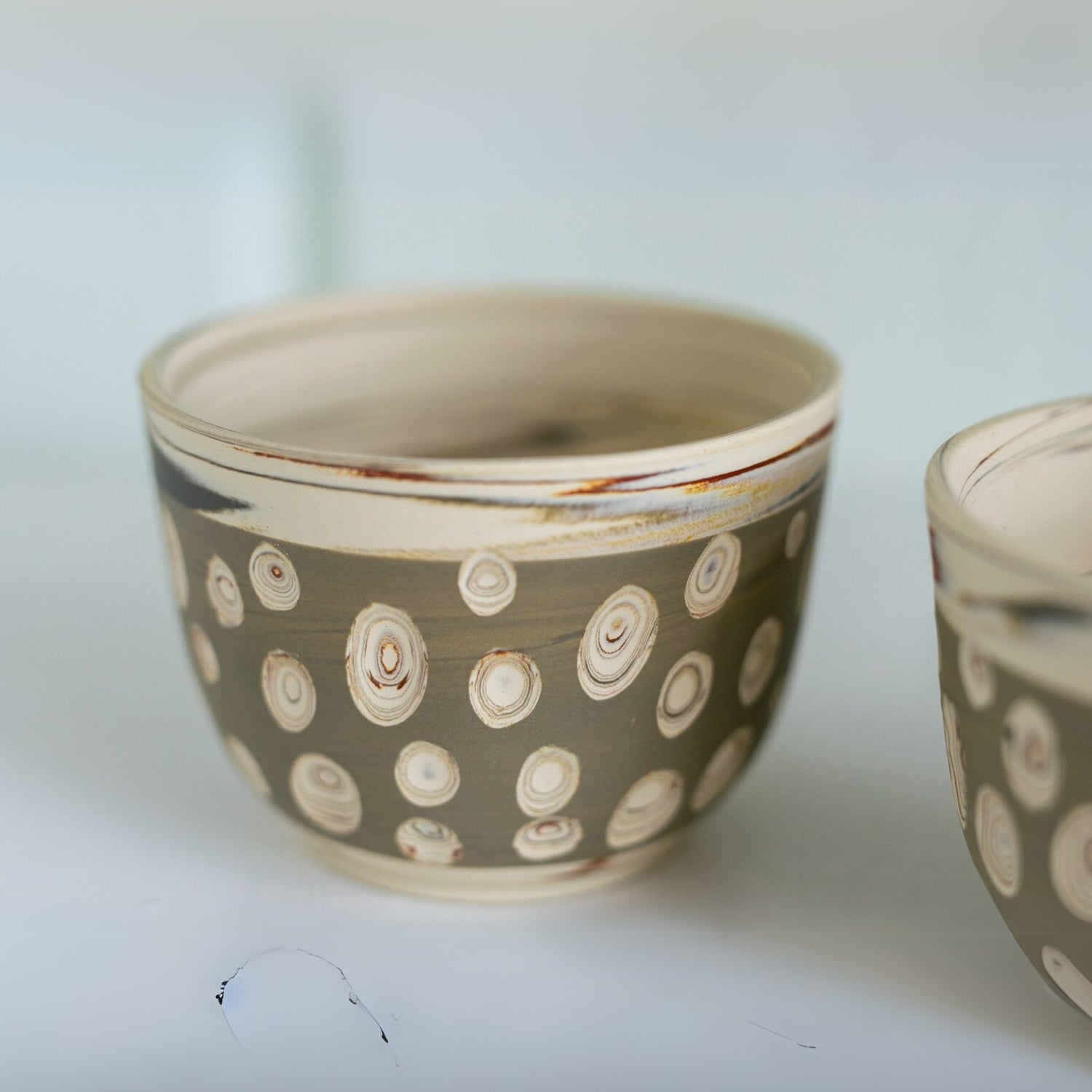 A ceramic bowl with a brown base and circular patterns in cream and light brown, evoking the elegant style of the Japanese Kyusu Set - Teapot with Filters (370ml) and Two Cups, is perfect for serving delicate green tea.