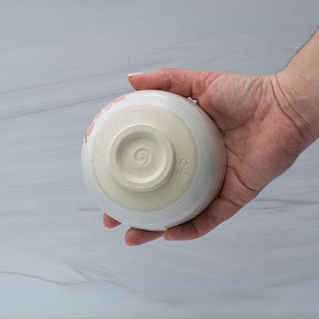 A hand holds an upside-down Maruyoshi Sakura Clay Matcha Bowl, showcasing a spiral design against a light background. This bowl, crafted with precision and elegance, reflects the timeless art of Japanese pottery.