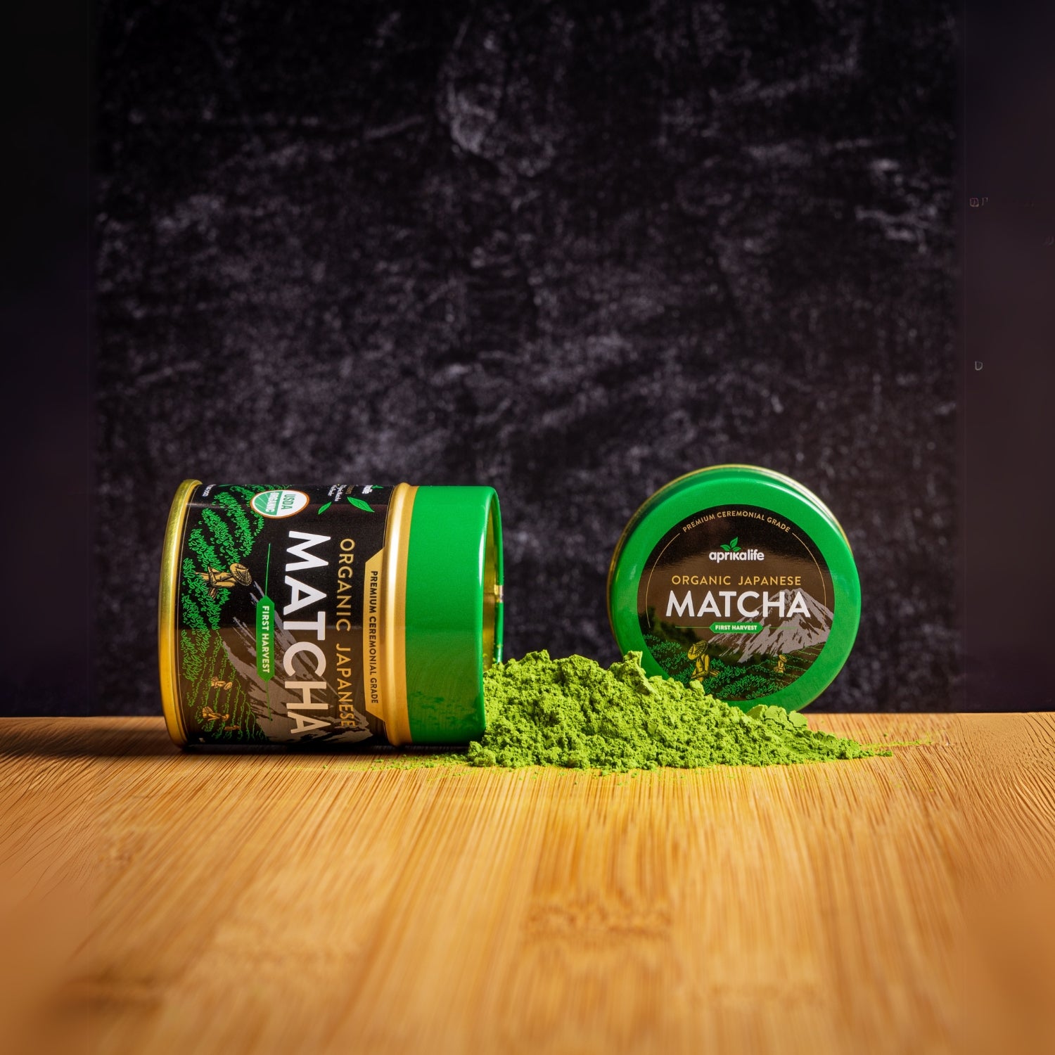 Two containers of Organic Japanese Ceremonial Grade Matcha Green Tea Powder, one open with bright green matcha beautifully scattered on a wooden surface.