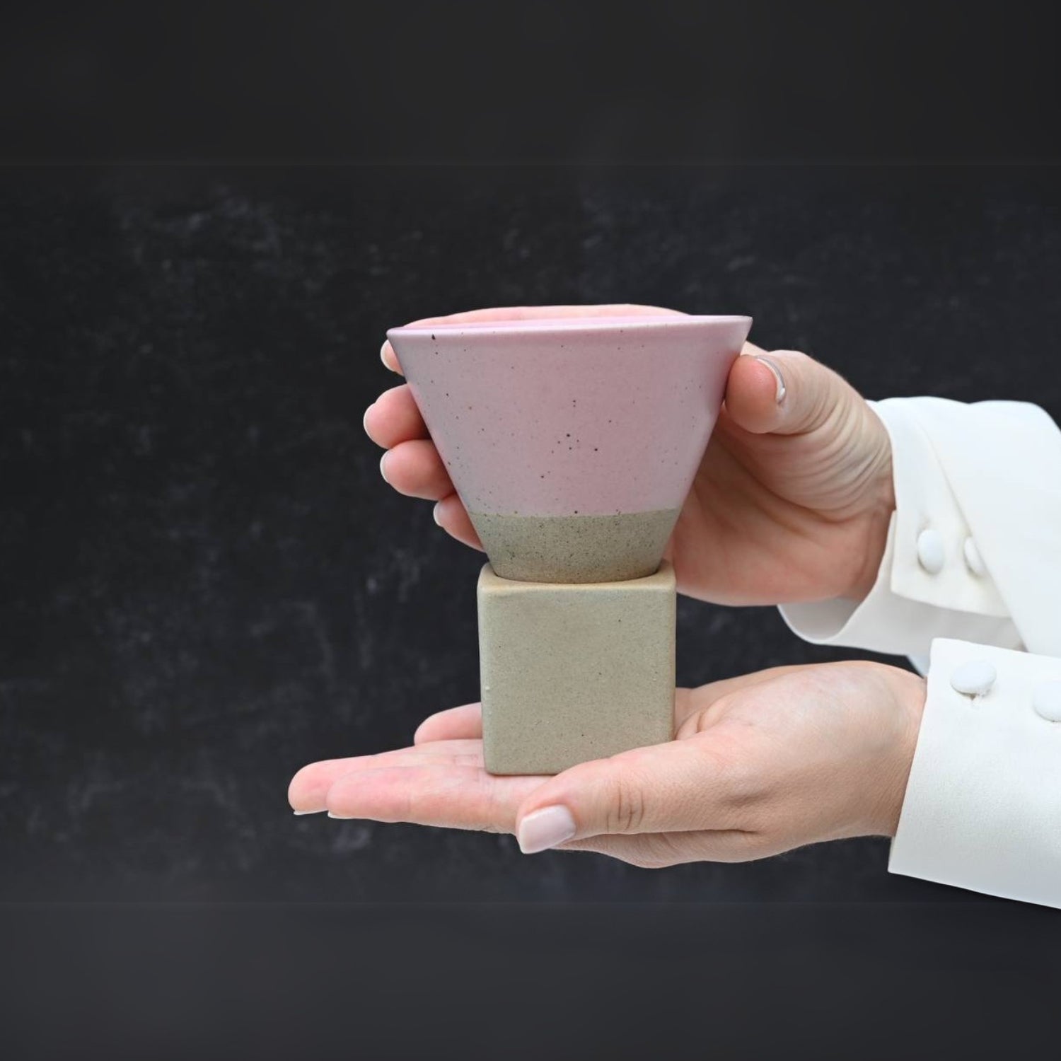Hands holding a Pink Coffee Mug with Base - 6.8 oz/200ml, showcasing exquisite ceramic artistry in pink and beige with a geometric design.