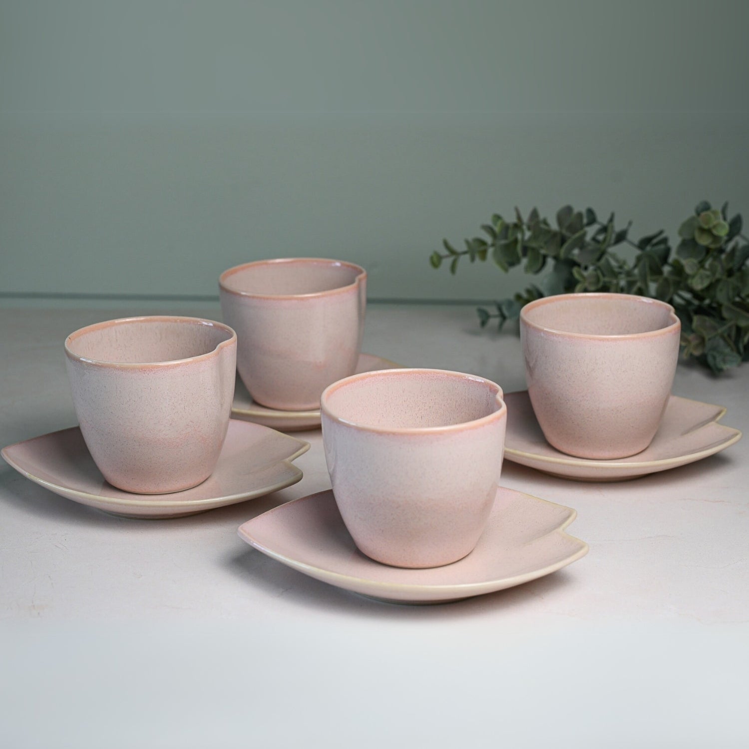 The Pink LOVE Ceramic Tea Cup with Saucer is a handcrafted set featuring four pink cups on square saucers. Perfect for sipping green tea, its elegant design evokes the simplicity of a Japanese Ippuku-wan Tea Cup, beautifully highlighted by lush greenery.