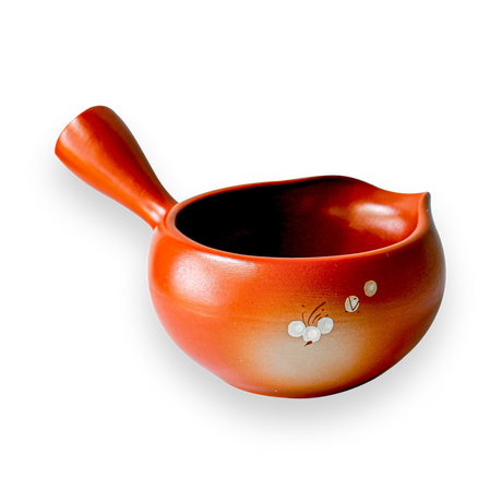 The Red Flowers Ceramic Matcha Bowl with Spout, featuring floral designs on a black background and a small handle, makes an elegant housewarming gift inspired by traditional Japanese tea ceremonies.