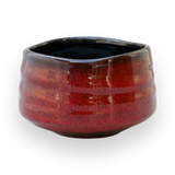 The Red Matcha Bowl features a red glaze and a rounded, slightly uneven shape, evoking the essence of traditional Minoyaki Pottery, set against a black background.