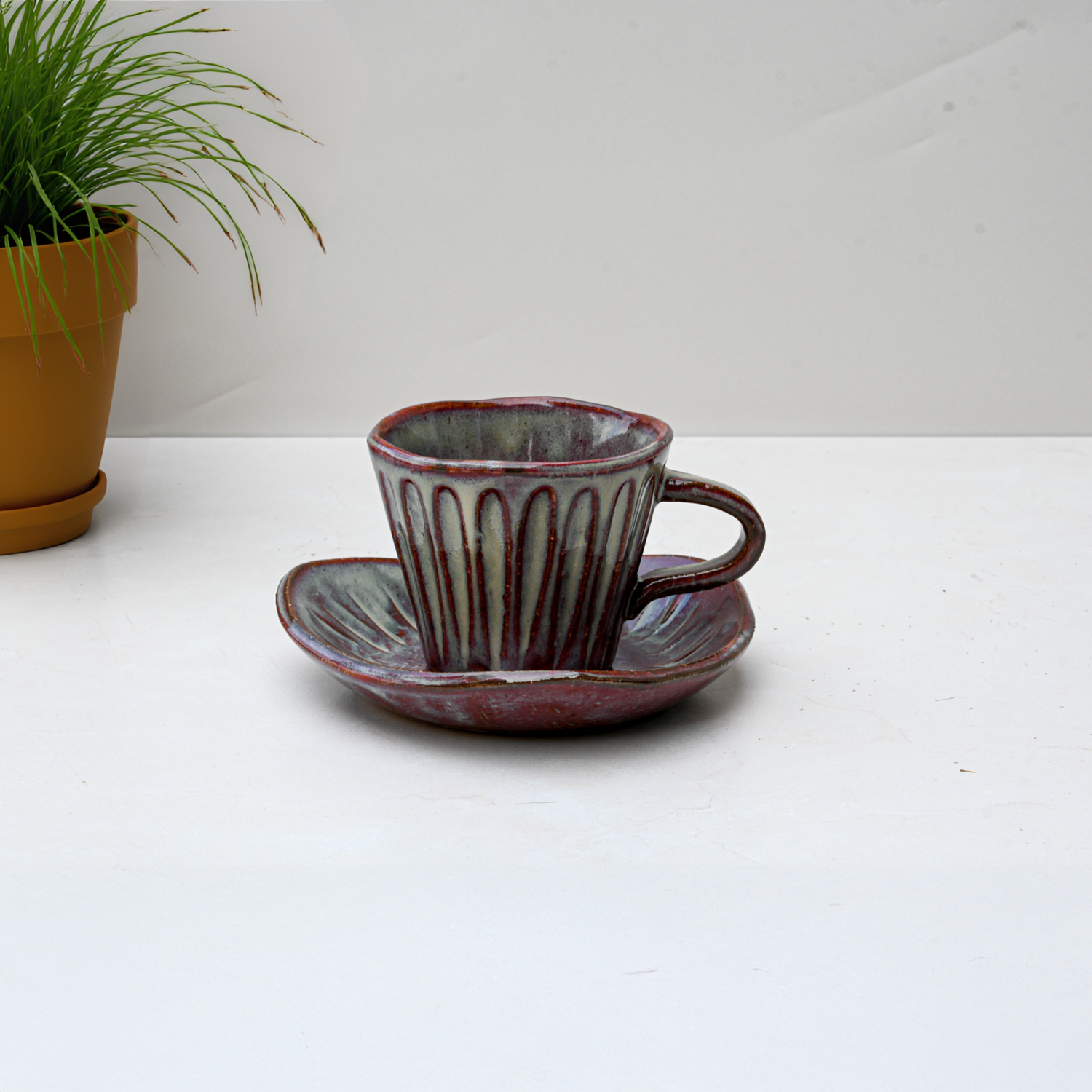 The Shibu Yunomi Japanese Tea Cup with Saucer sits on a white surface, complemented by a nearby potted plant for a cozy, inviting display.