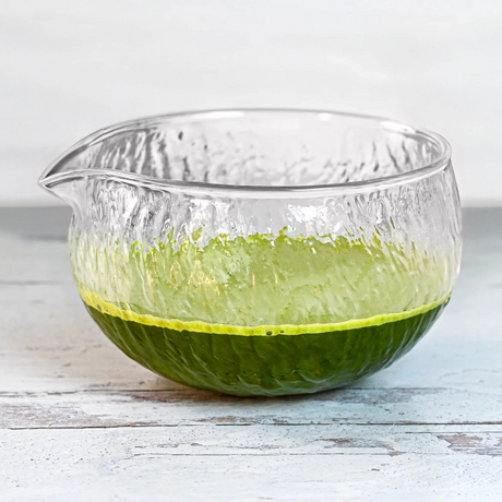 The Textured Spouted Glass Matcha Bowl Pattern 2, filled halfway with vibrant green matcha, rests elegantly on a light wooden surface.