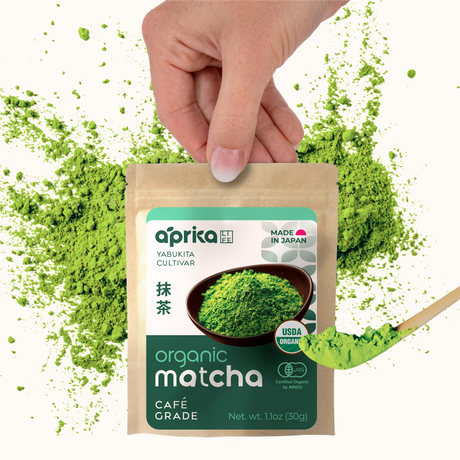 A hand holds a spoon over a packet of FREE Japanese Matcha Green Tea Powder (1.05 oz/30g) with vibrant green matcha powder scattered around.